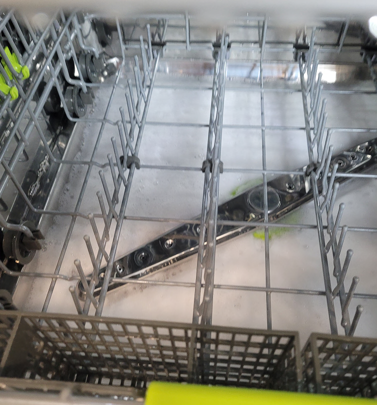 Inside view of a dishwasher with wire racks, spray arms, and suds.