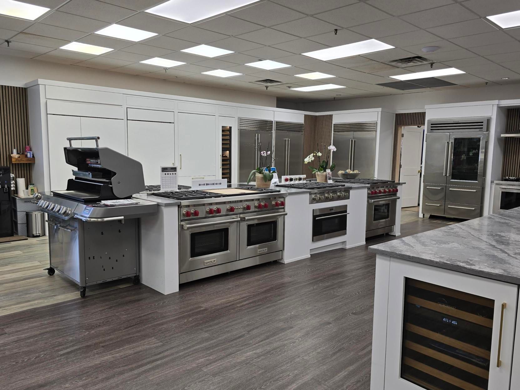 Kitchen appliance showroom with stainless steel ovens and refrigerators on display.