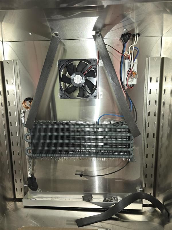 Inside of a stainless steel appliance, a cooling coil with a fan, wiring, and insulation.