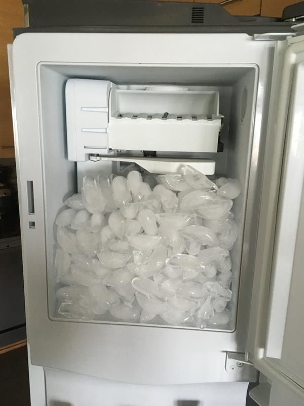 Ice dispenser in a white refrigerator, filled with ice.