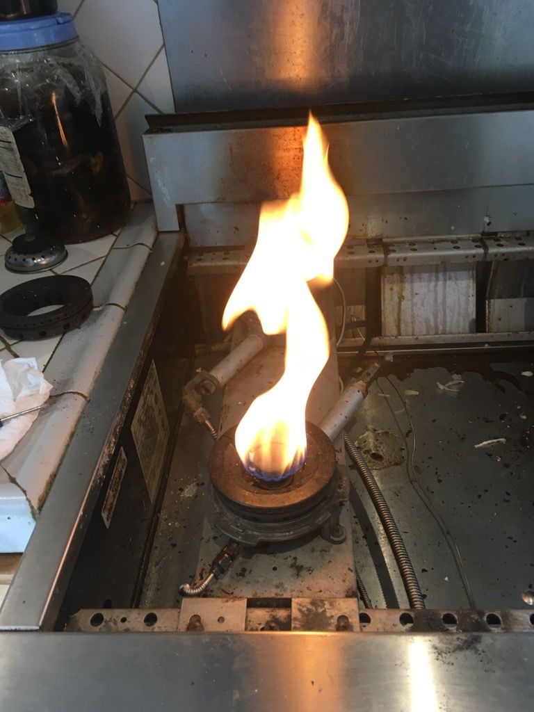 Burning gas stove burner in a stainless steel kitchen, flame orange and blue.