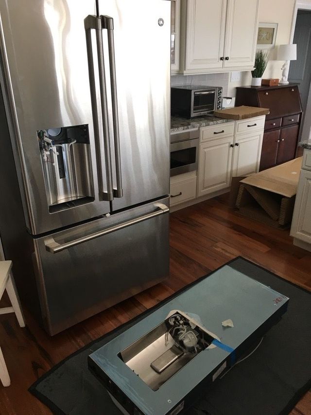 Stainless steel refrigerator next to a kitchen countertop with an open drawer on the floor.
