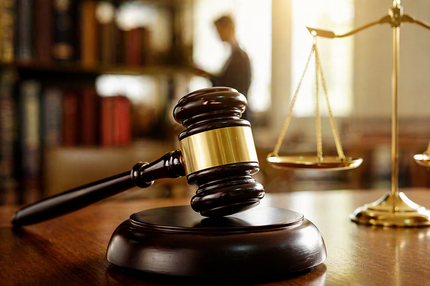 Judge’s gavel on a wooden desk with gold scales of justice in a law library setting
