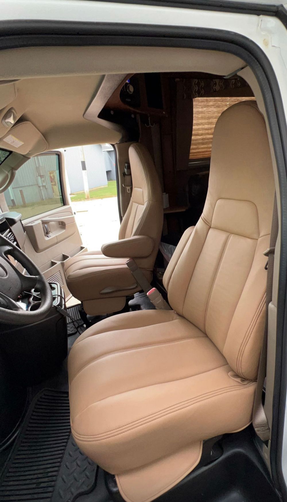 Interior of a van, showing tan captain's chairs, steering wheel, and a view to the outside.