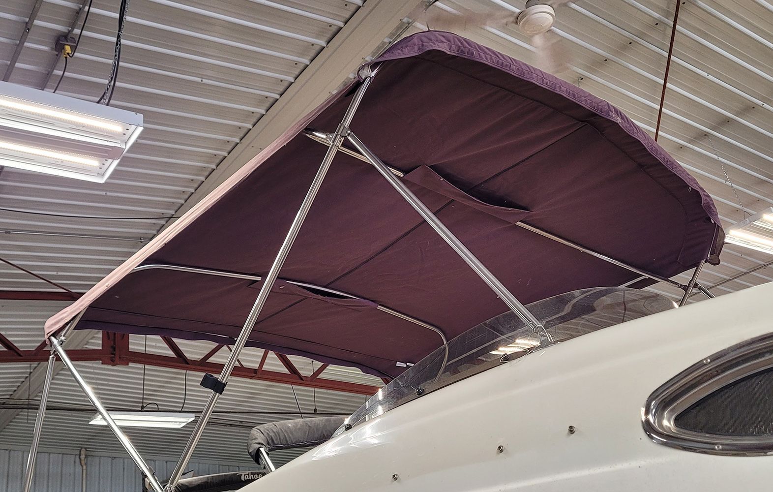 Maroon boat canopy on a white boat in an indoor setting.