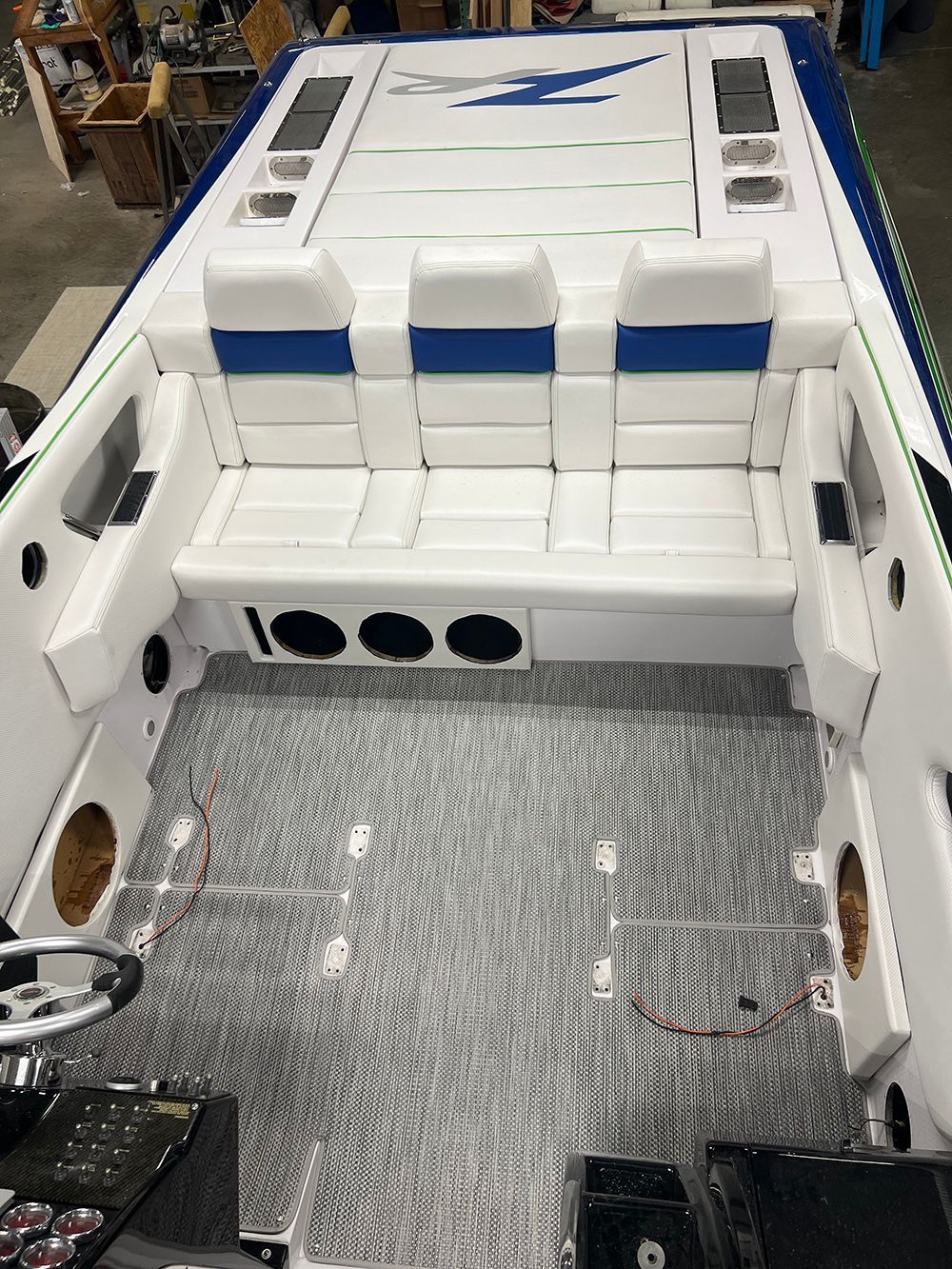Boat interior with white seats, blue accents, black speakers, and gray flooring.