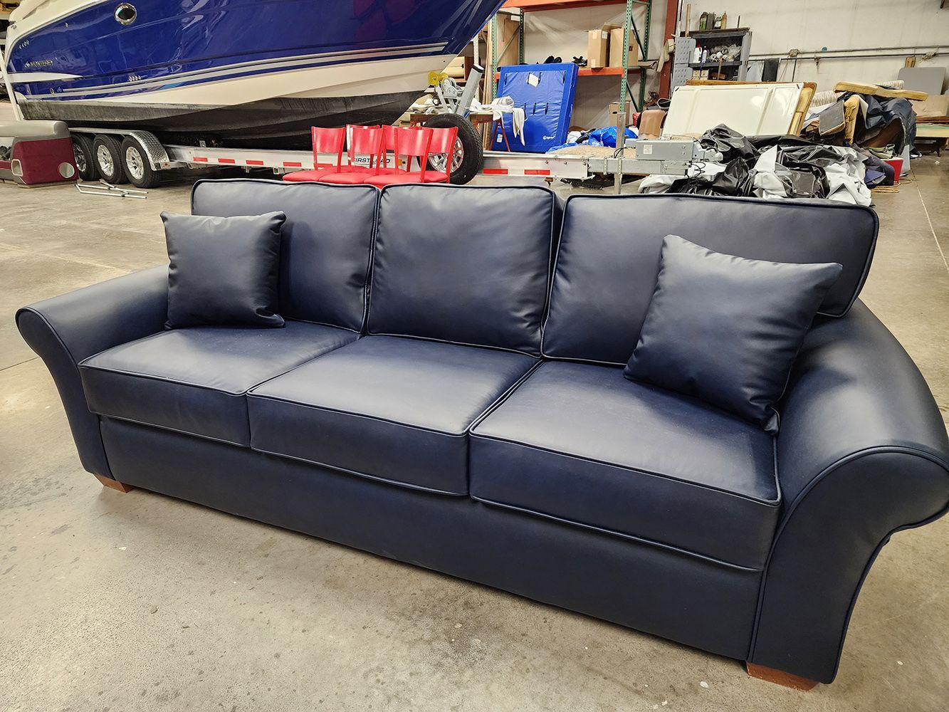 Blue leather sofa with two pillows, in a workshop setting with a boat in background.