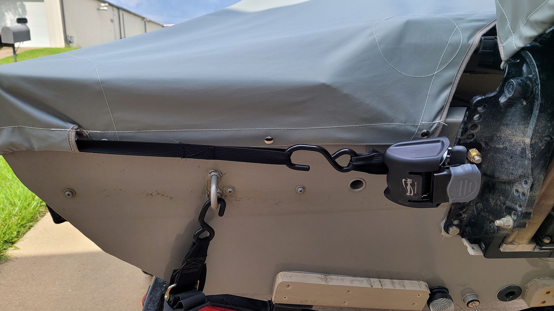 Boat's stern with gray tarp cover secured by a black bungee cord. A trailer hitch is visible on the right.