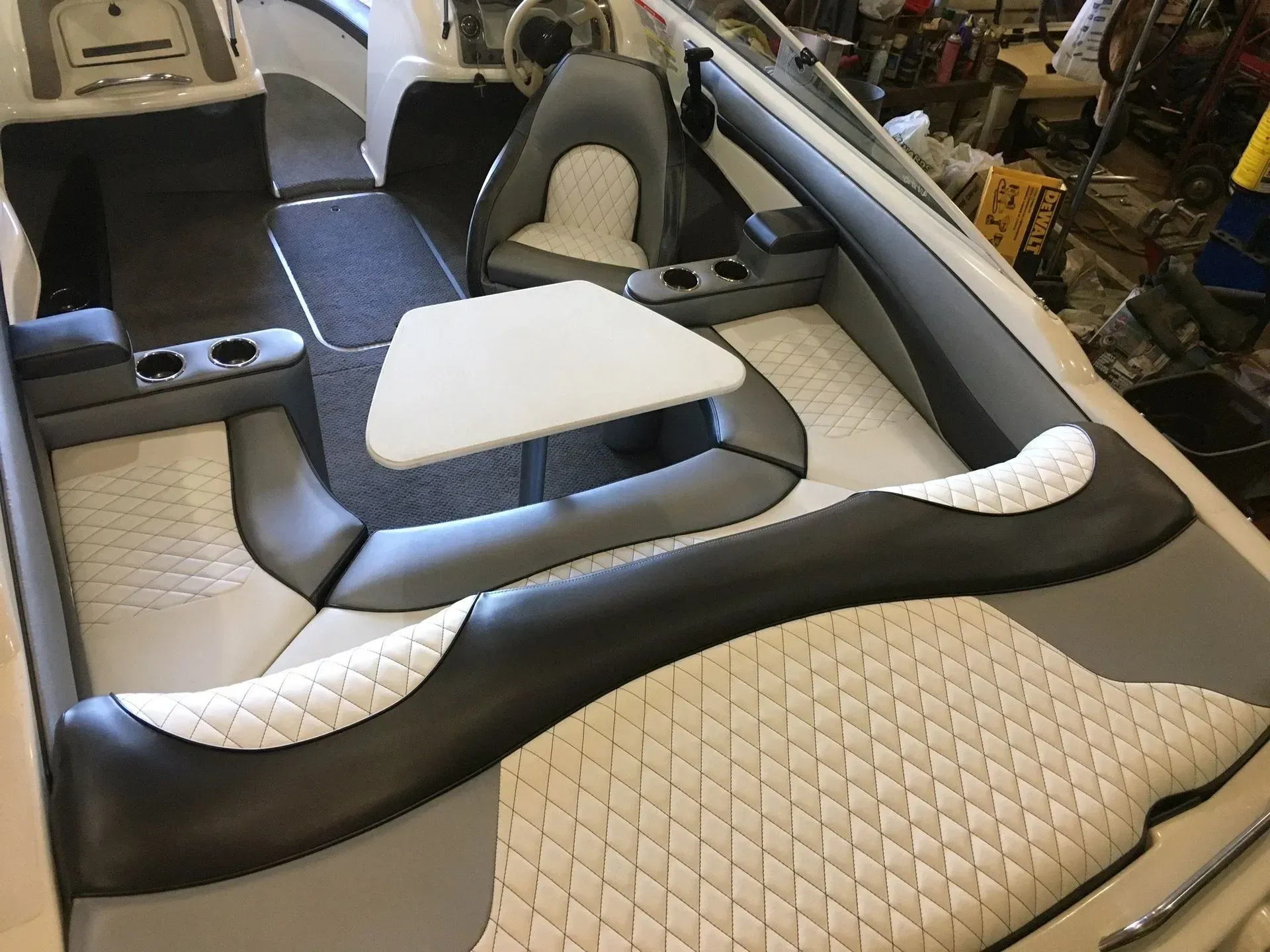 Boat interior with gray and white diamond-stitched upholstery, a table, and cup holders.