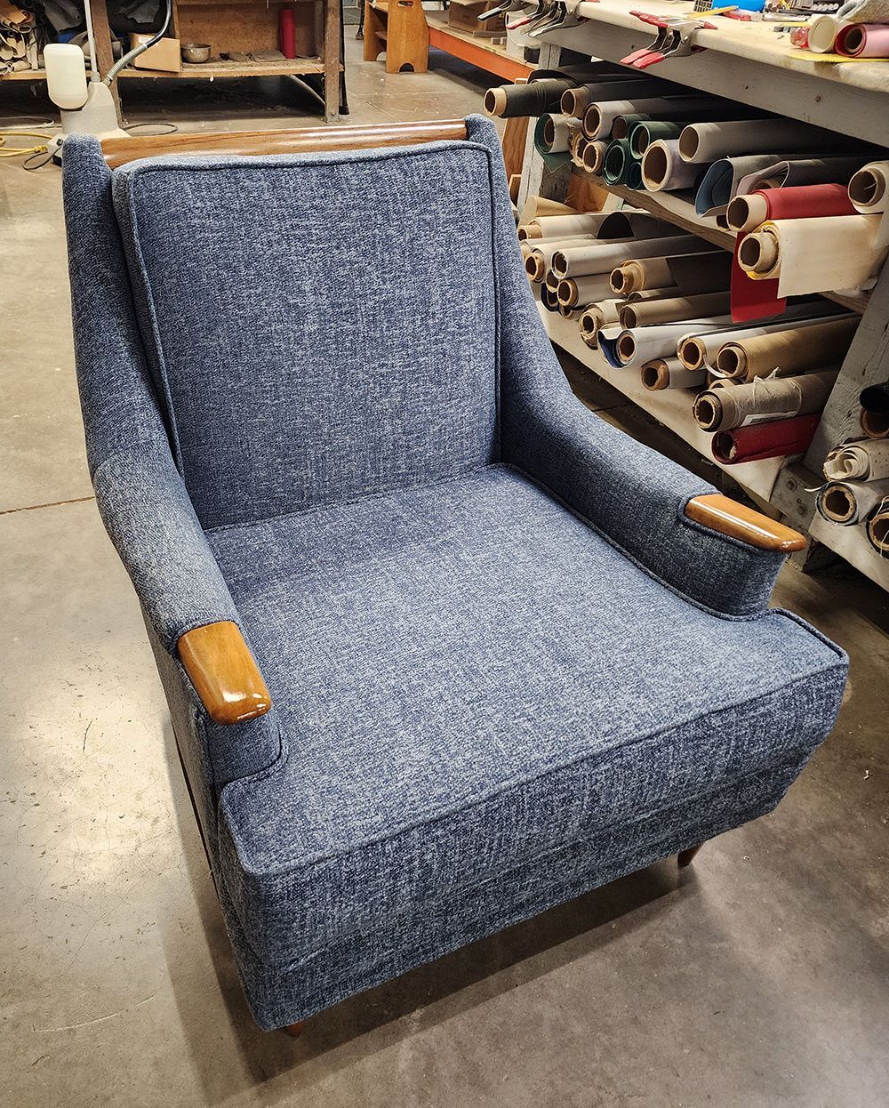 Blue upholstered armchair with wood trim and armrests in a workshop setting.