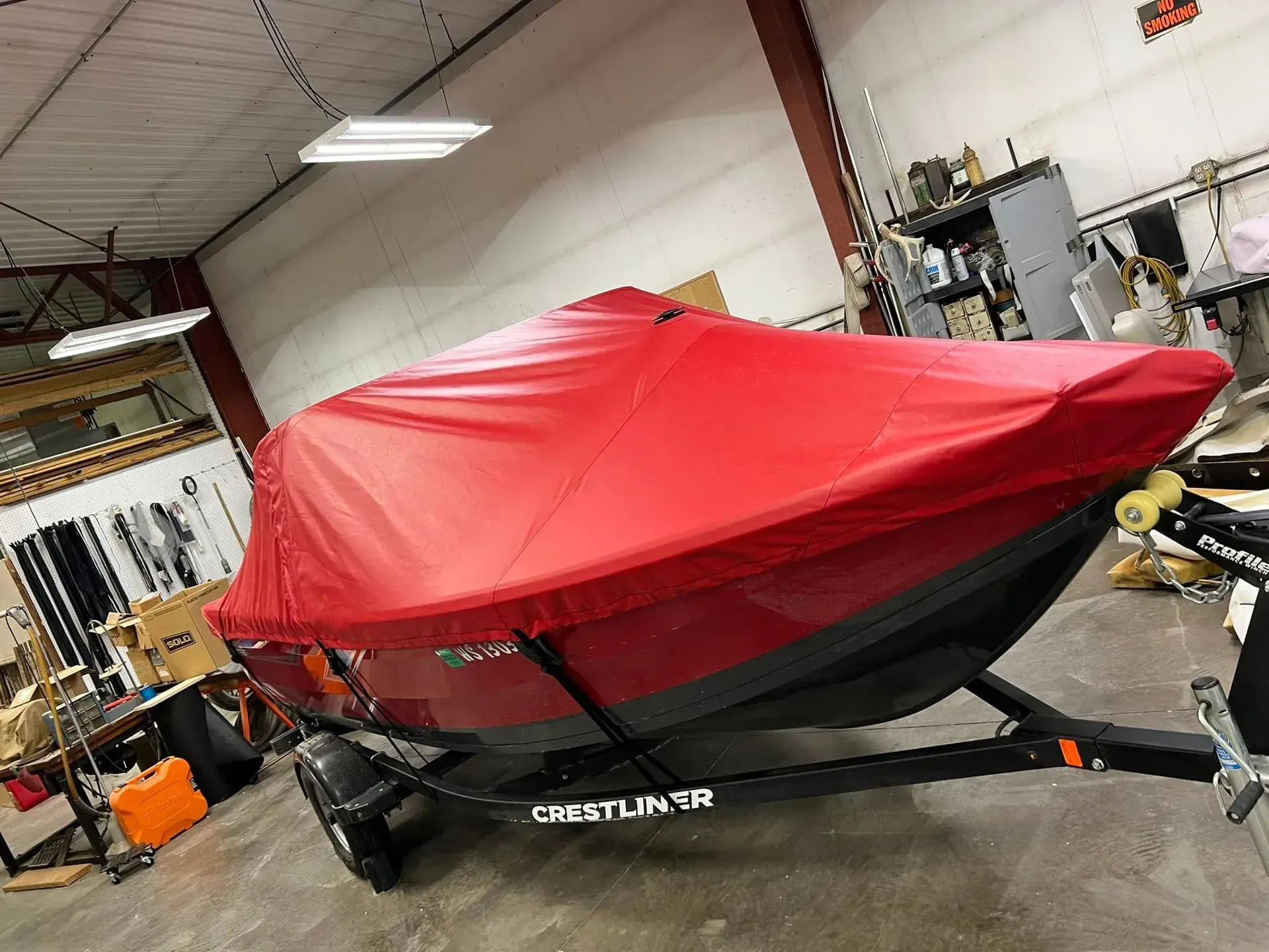 Red boat covered on a trailer, inside a workshop.