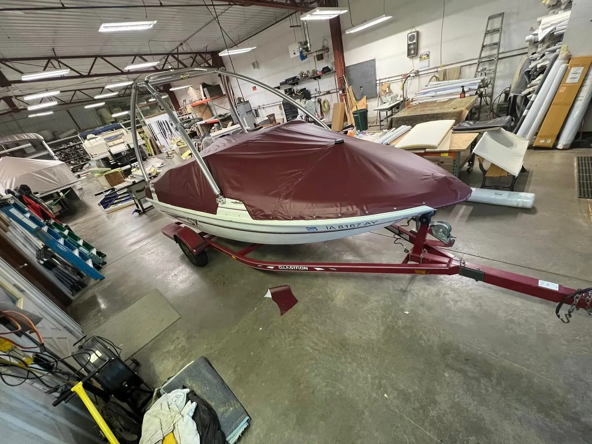Boat on a trailer in a workshop, covered in a burgundy tarp.