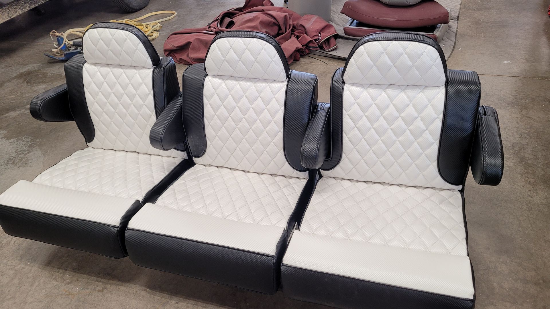 Three-seat row with white diamond-stitched upholstery, black trim and armrests, on a cement floor.