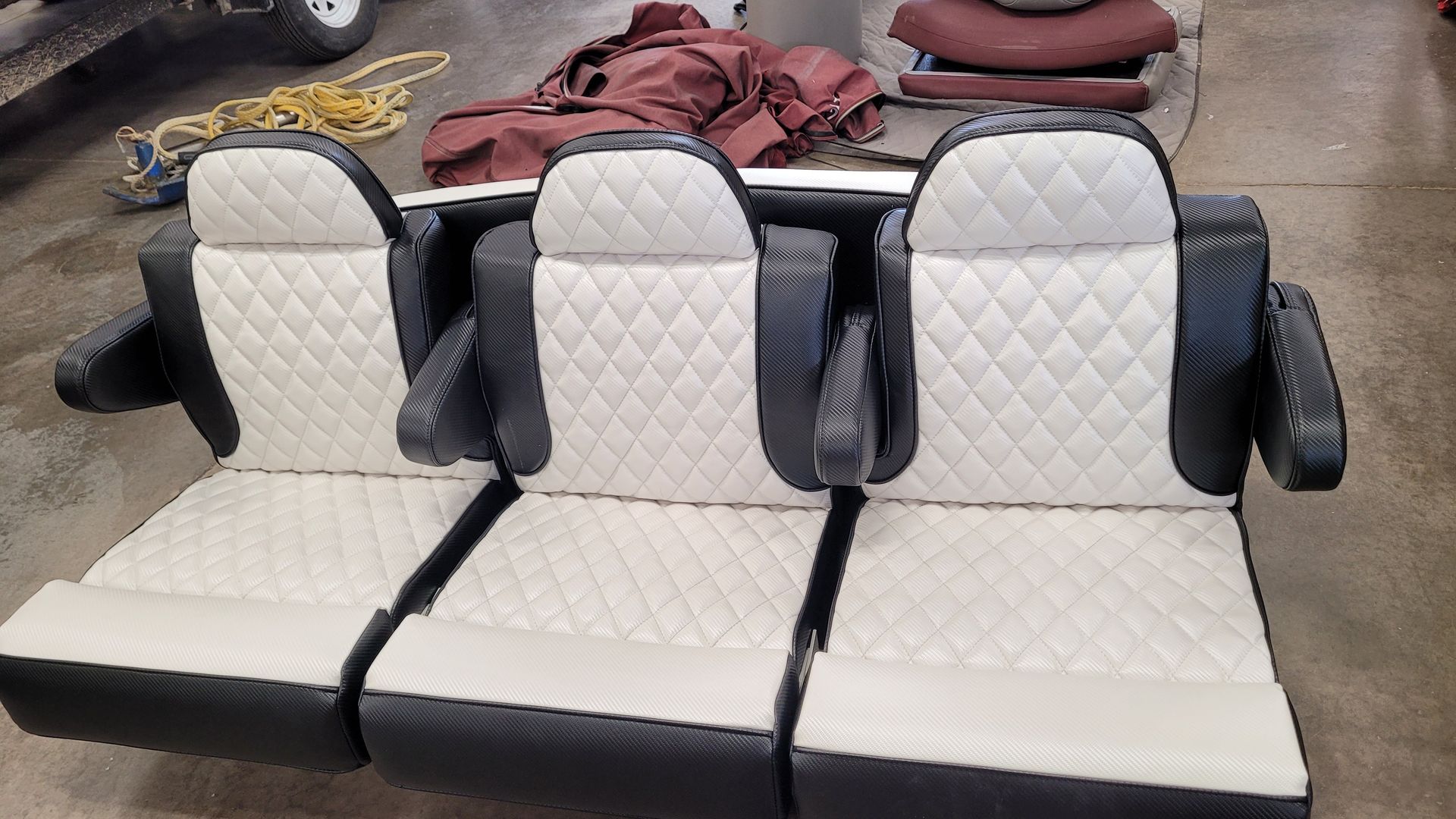Three cream and black boat seats with diamond-stitched cushions and armrests, sitting on a concrete floor.