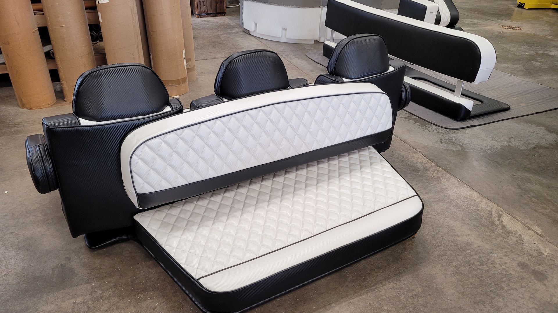 Black and white quilted car seats, possibly for a vehicle, arranged in a factory setting.