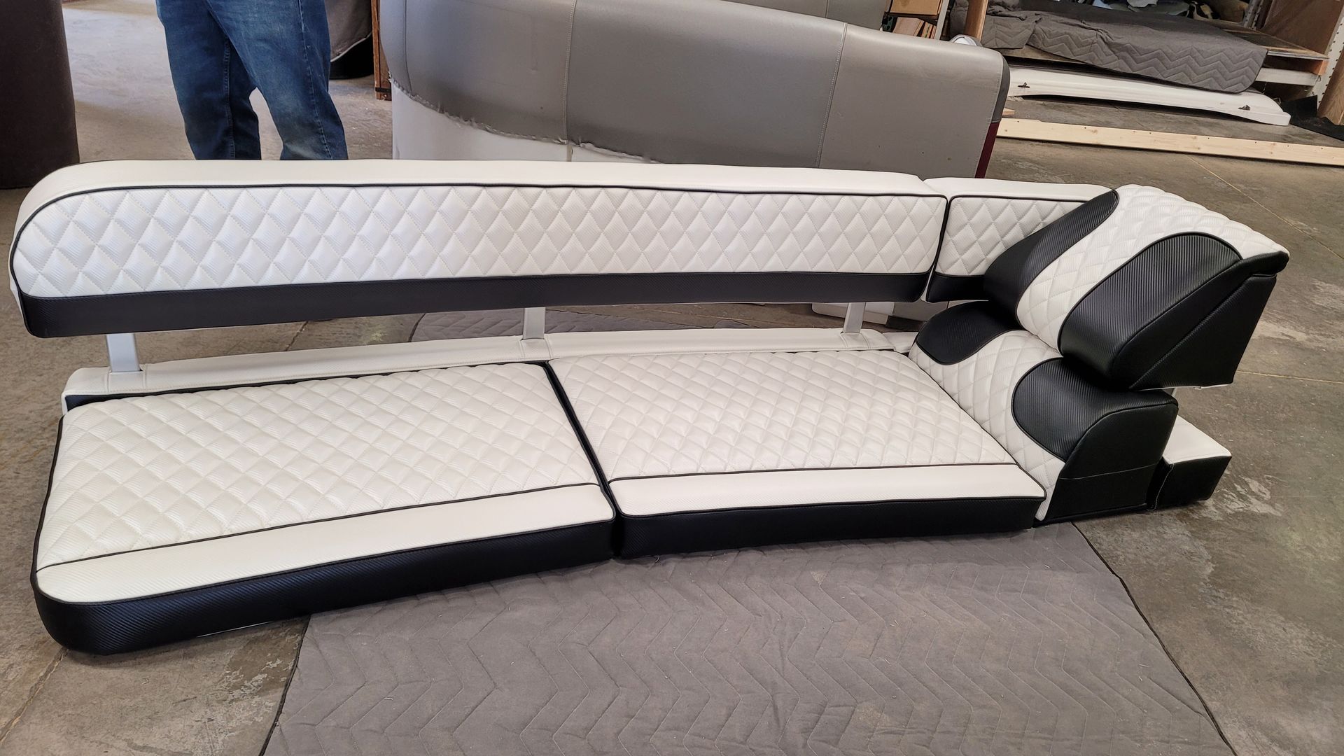 White and black quilted boat seating on a gray floor with a partial view of a person.