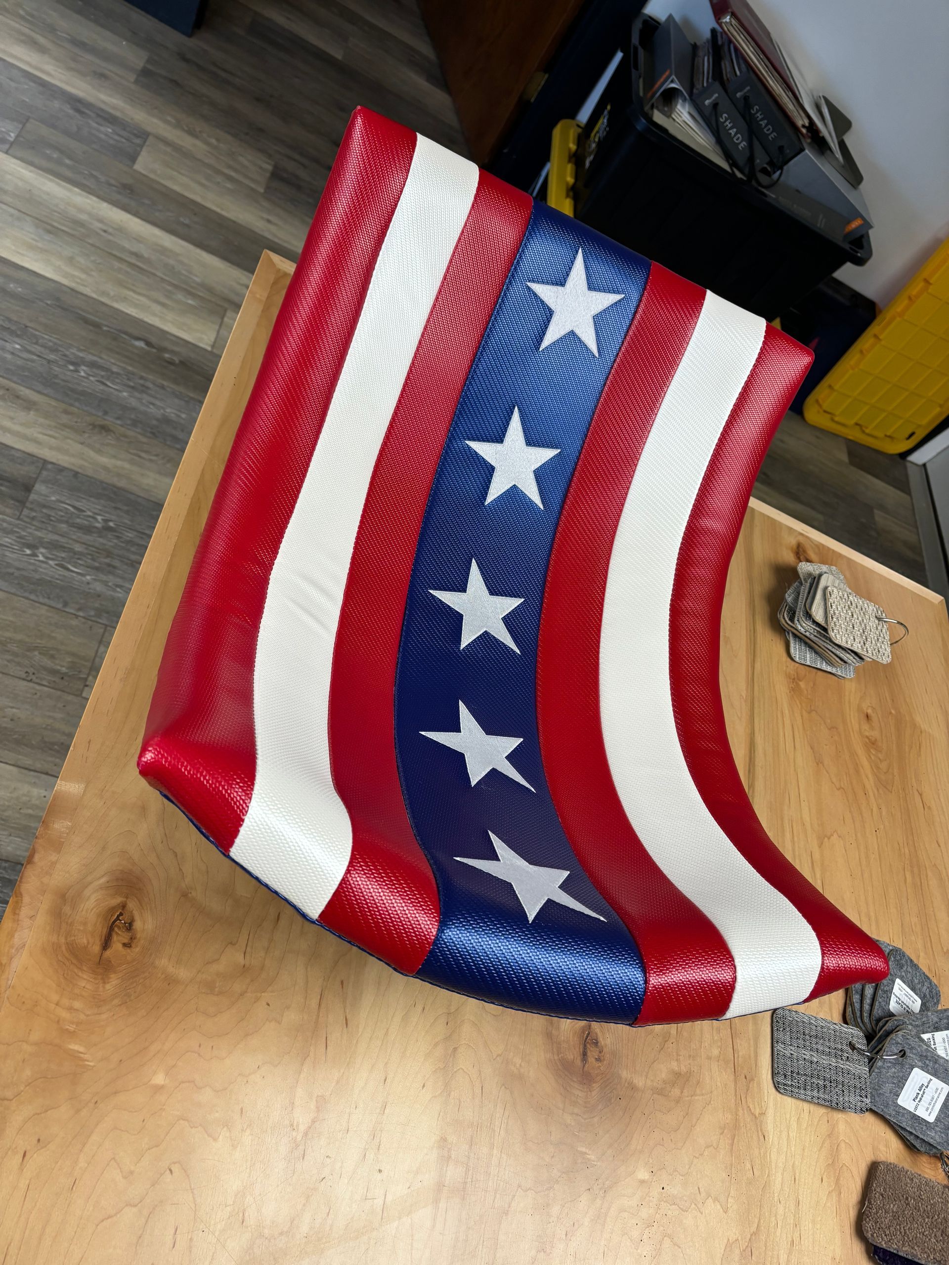 American flag-patterned cushion on a wooden table. Red, white, and blue stripes with white stars.