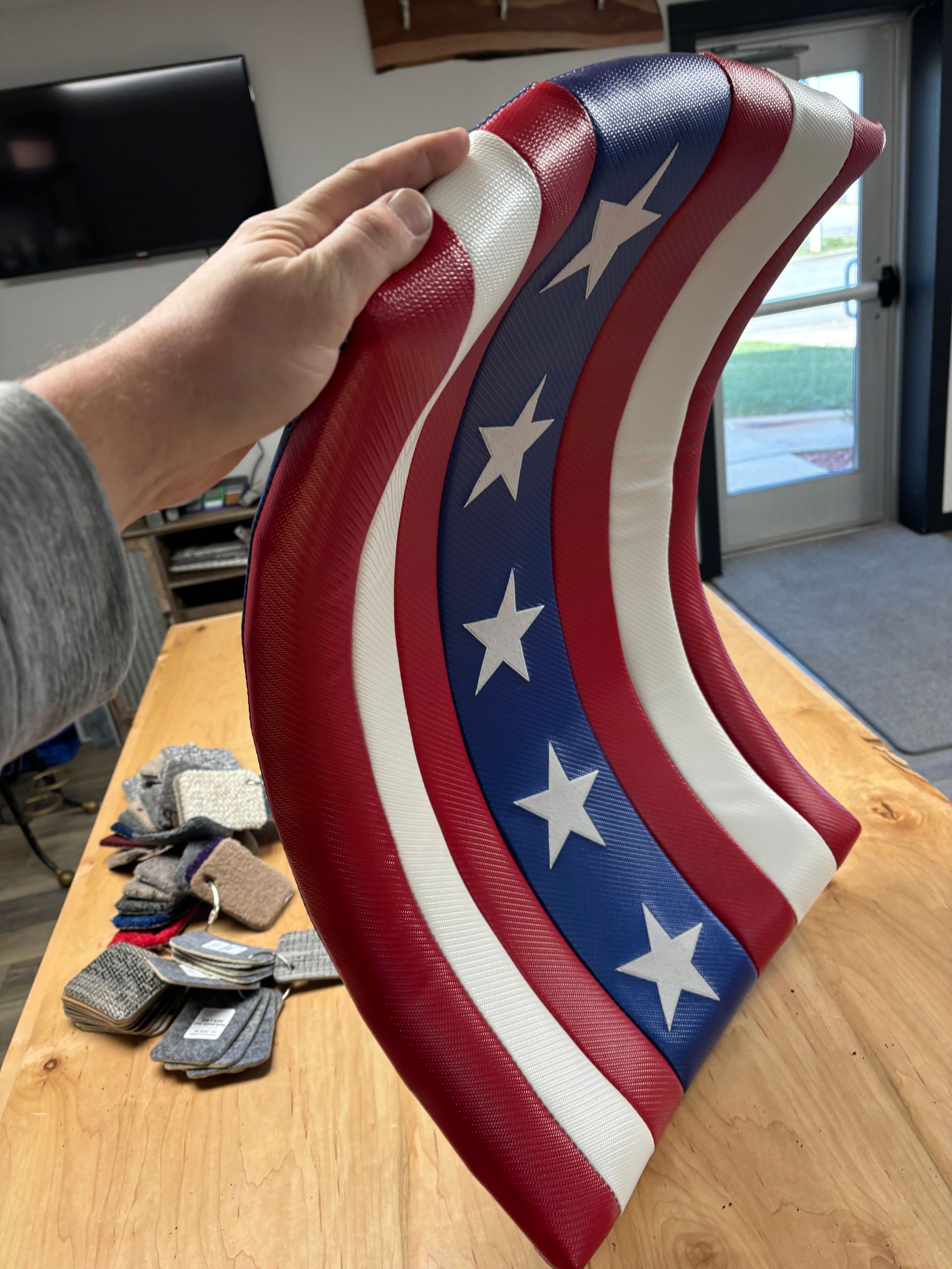 Hand holding a curved leather American flag art piece, red, white, and blue, with white stars.
