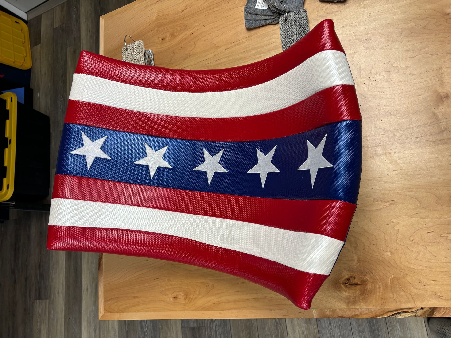 Red, white, and blue American flag-inspired shield with white stars and curved stripes, resting on wood surface.