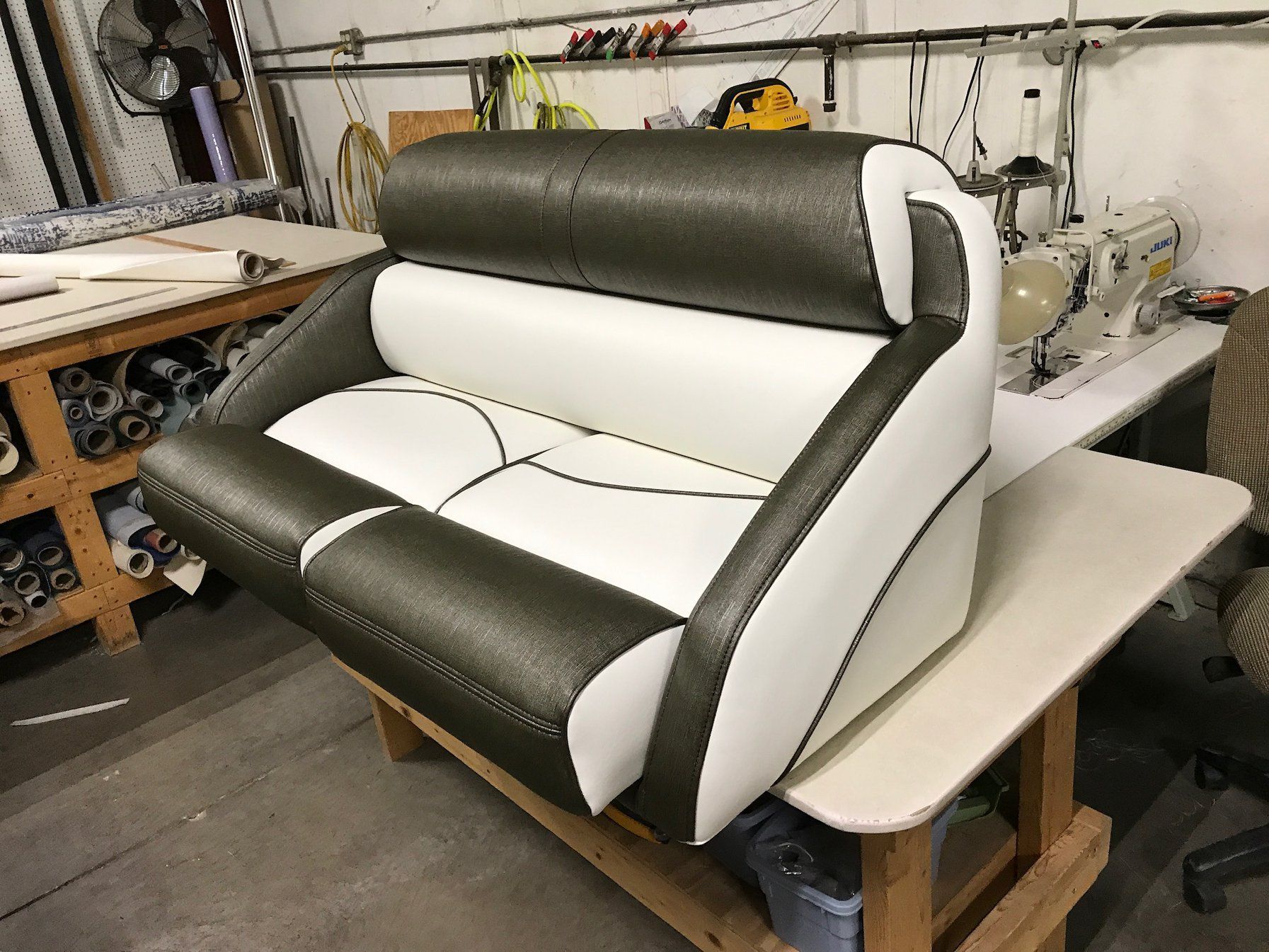 A two-toned boat seat, white and dark gray, sits on a wooden work table in a shop.