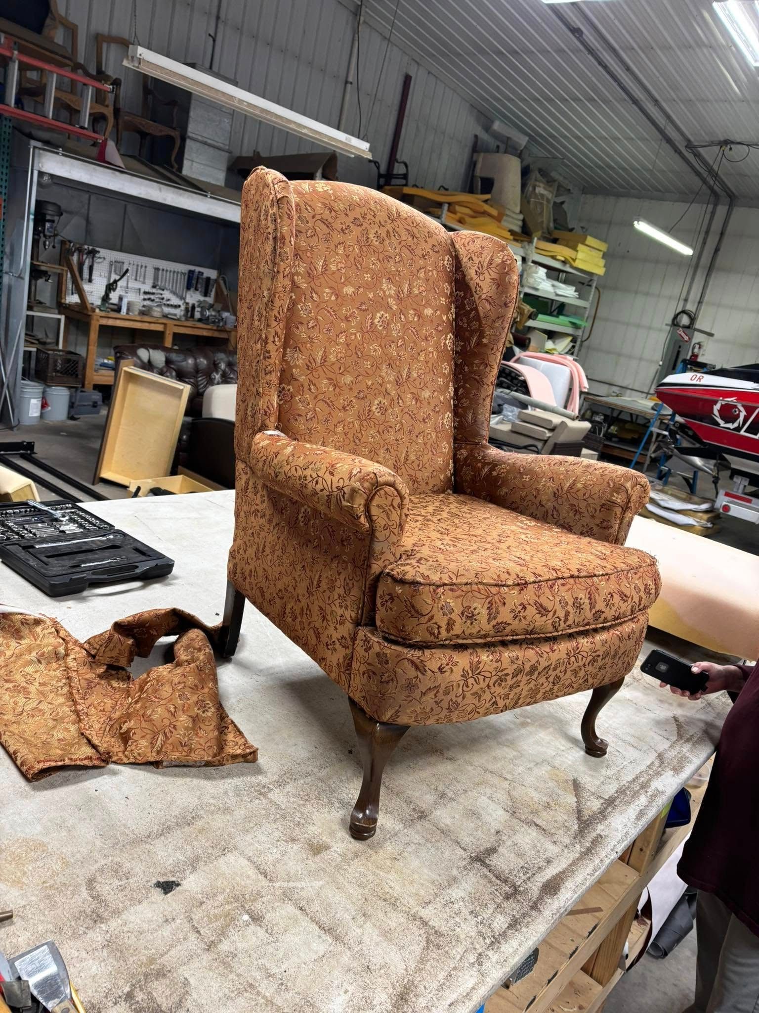 Wingback chair in a workshop, undergoing upholstery work, brown patterned fabric.