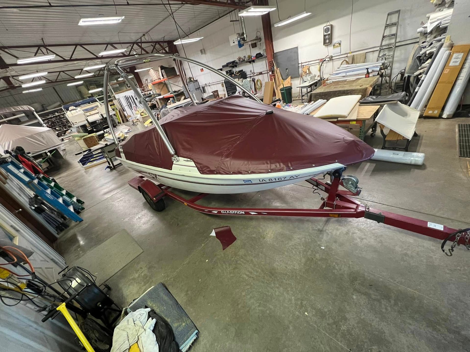 Boat on a trailer in a workshop, covered by a burgundy tarp.