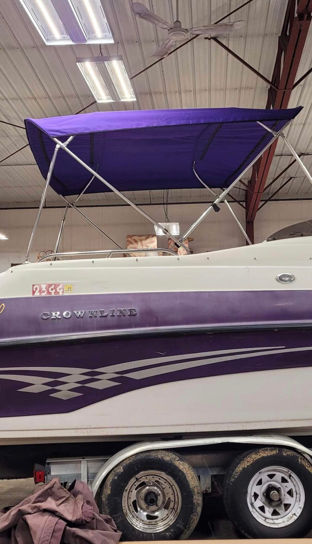 Purple-canopied Crownline boat on a trailer, indoors.