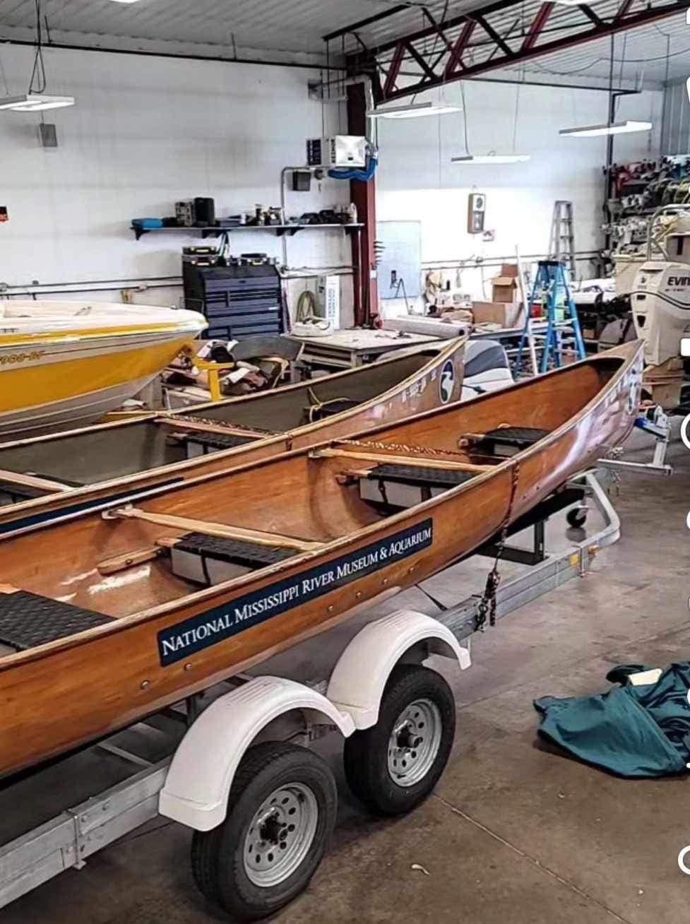 Wooden canoes on a trailer inside a workshop. One has a National Museum label.