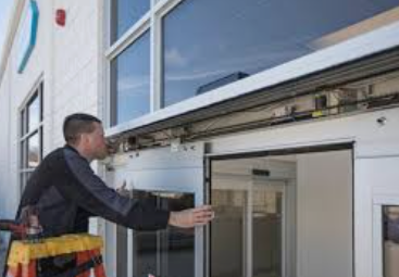 A man is standing on a ladder fixing a sliding glass door.