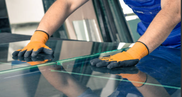 A man wearing gloves is cutting a piece of glass.