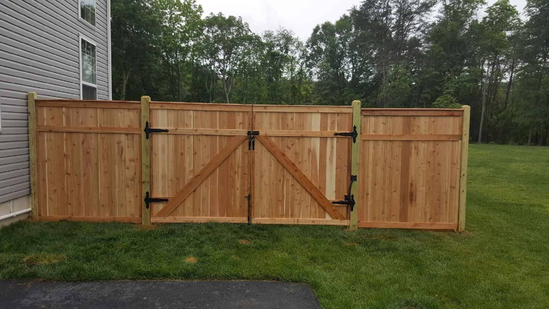 Wooden privacy fence with double gate, in a grassy yard, near a building.