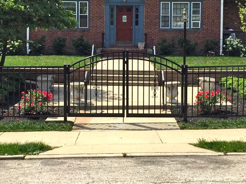 Black wrought iron gate leading to a brick building with steps. Landscaped front yard with flowers.