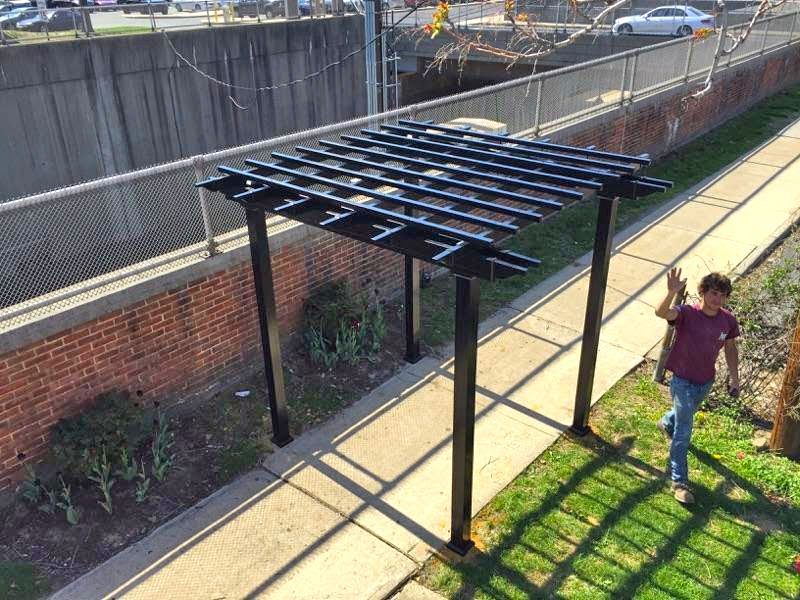 A person walks by a black pergola on a sunny day.