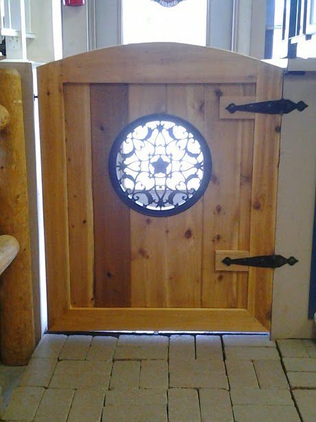 Wooden gate with circular decorative window, black hinges, installed on a brick floor.