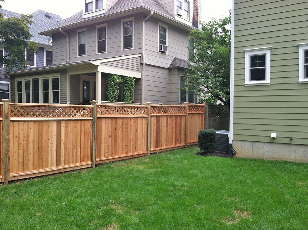 Wooden fence in a backyard with a grass lawn, next to a house with an air conditioning unit.