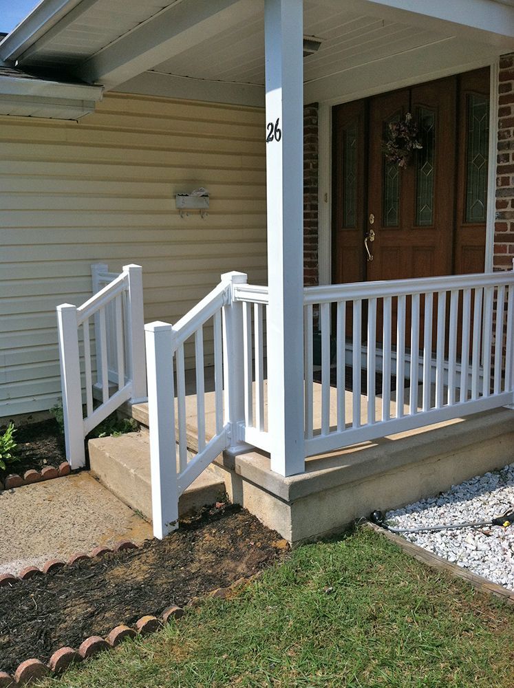 White porch with railing and steps leading to a front door with a wreath.