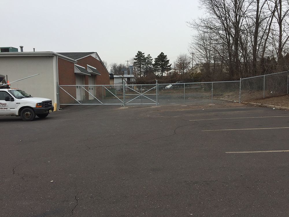 A gated parking lot with a white truck and a building in the background. The sky is overcast.