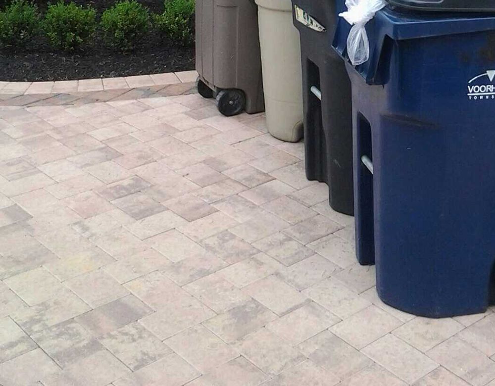 Four trash bins of various colors (brown, beige, black, and blue) lined up on a patterned stone patio.