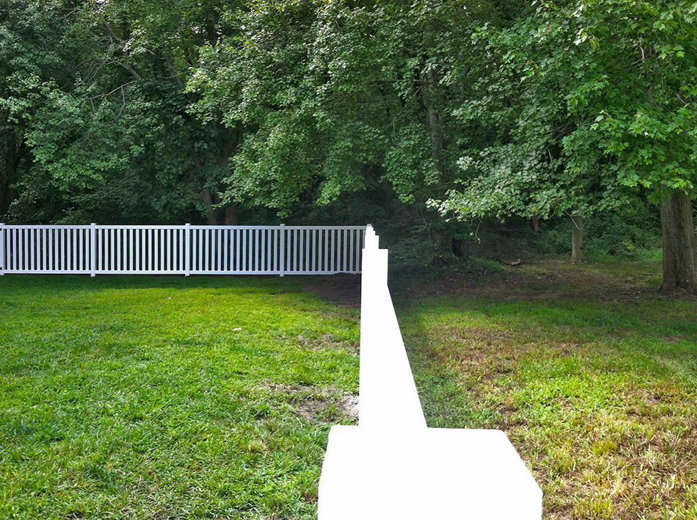 White picket fence bordering green lawn and forested area.
