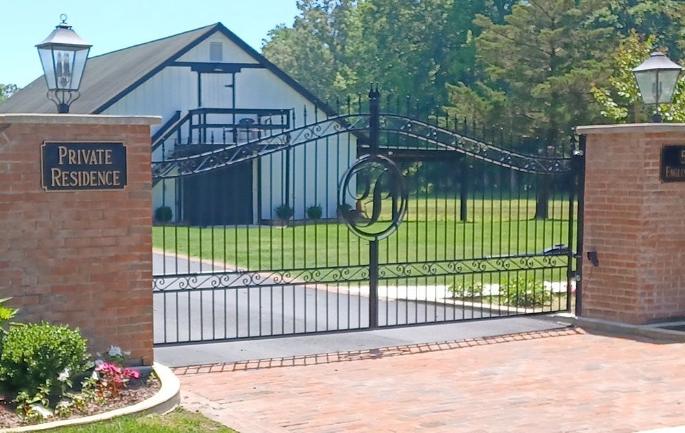 Black iron gate at a brick entrance to a private residence with a white building in the background.