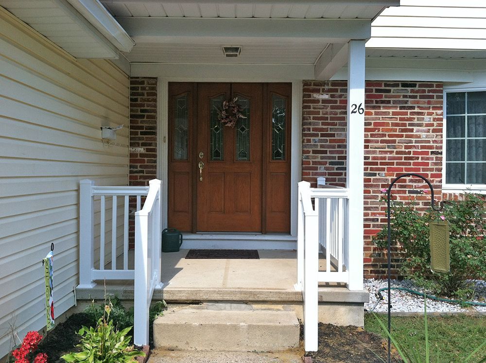 Front entrance of a house with brown door, white railings, and brick and siding exterior.