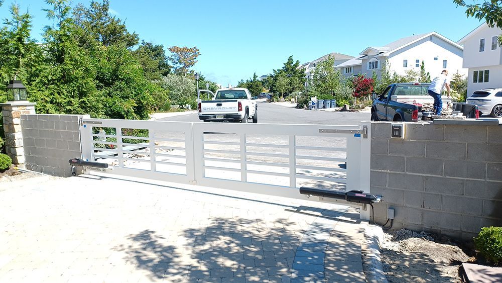 White gate across a driveway, with a truck passing through, light blue sky.