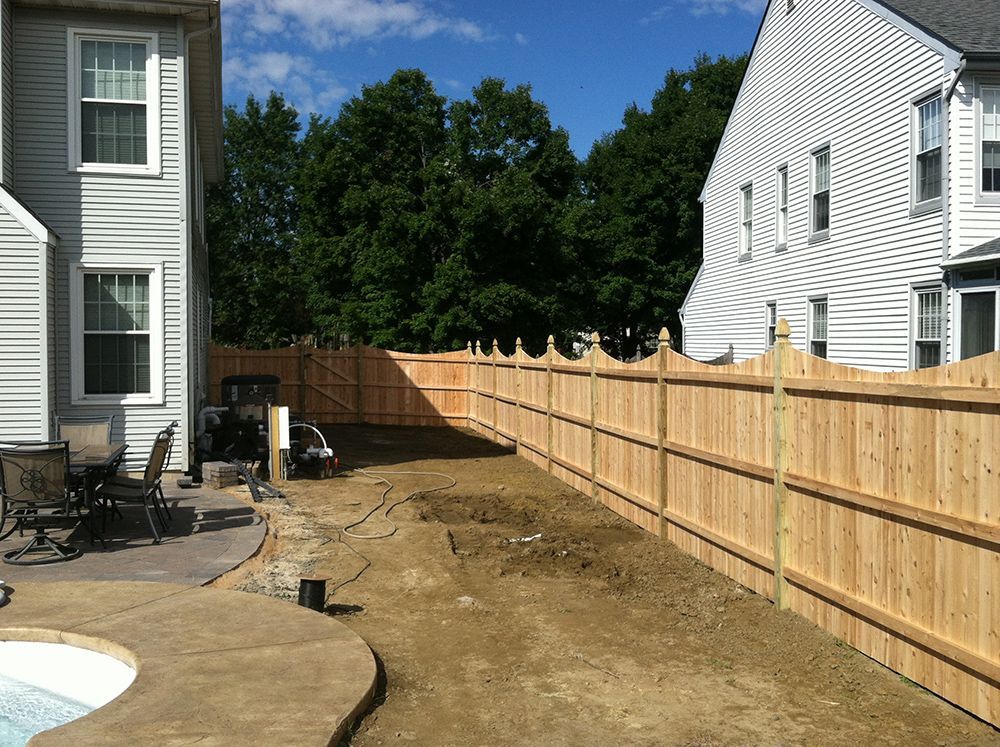 Backyard with wooden fence, concrete patio, dirt, and two-story houses.