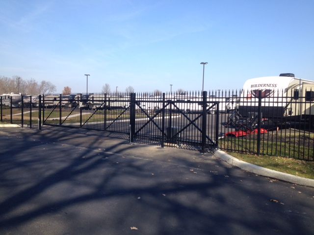 Black metal gate with pointed tops. RVs are parked in the background on a sunny day.