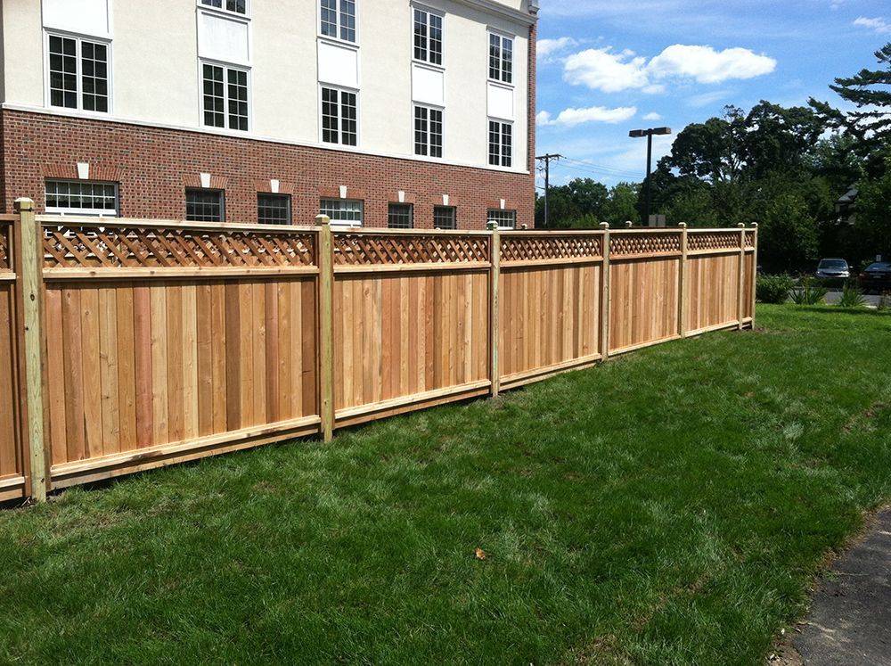 Wooden fence bordering a grassy lawn next to a brick building on a sunny day.