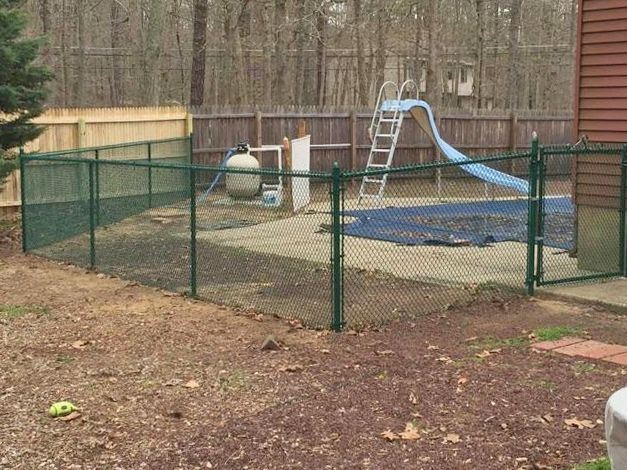 Green chain-link fence surrounds a backyard pool with a slide.