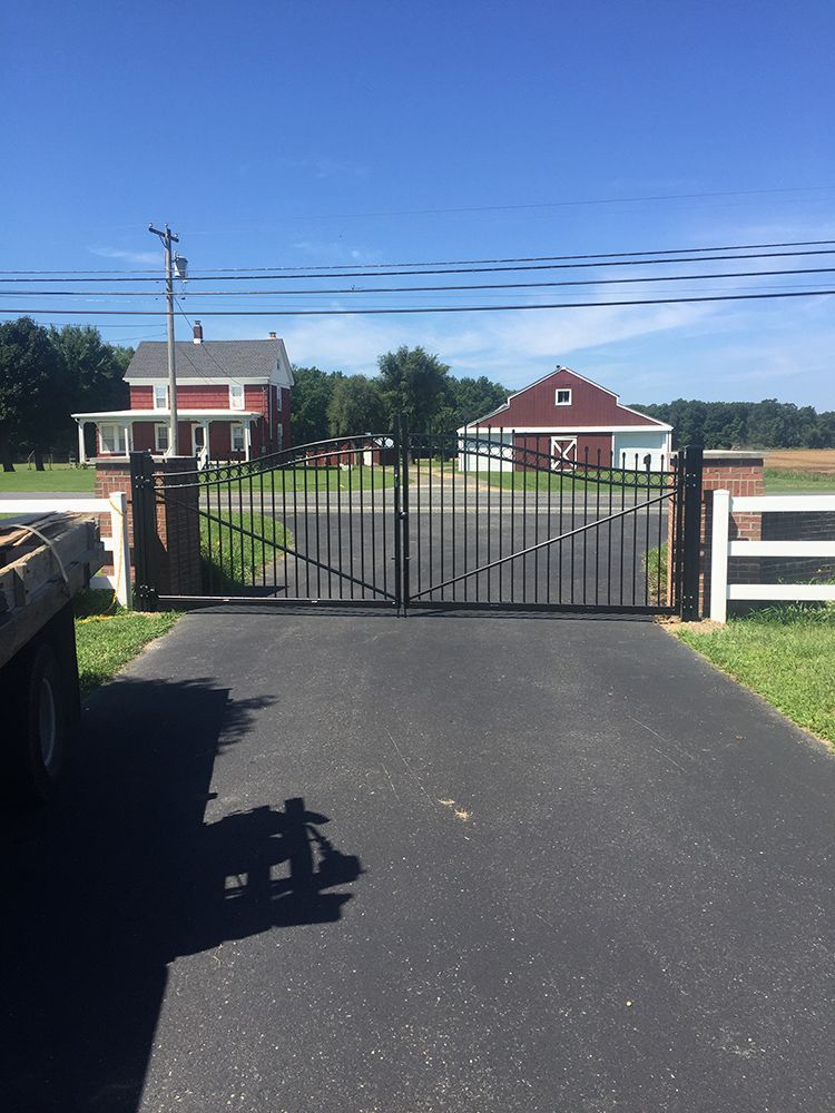 Black gate at a farm entrance with red buildings and a clear blue sky.