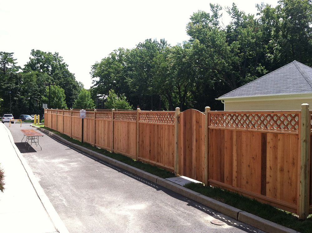 A newly constructed wooden fence alongside a street, separating the road from property, with trees in the background.