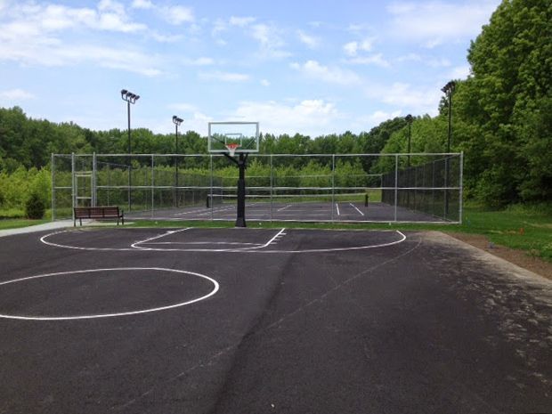 Basketball court enclosed by fencing, with a hoop and surrounding trees under a blue sky.