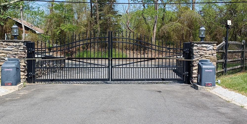 Black metal gate with stone pillars at a driveway entrance. Automatic gate opener on each side.